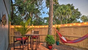 Une terrasse avec une table et des chaises en bois, un hamac et une clôture en bois décorée de guirlandes lumineuses.