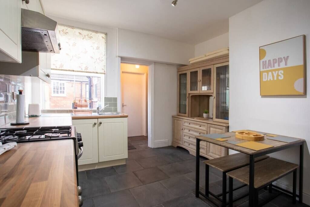A modern kitchen with a gas stove, white cabinets, and a dining area with a wooden table and benches.