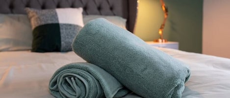 A neatly made bed with a folded towel and a lamp on the side.