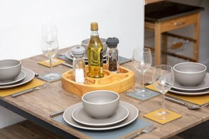 Een houten eettafel gedekt met borden, kommen, glazen en een fles olijfolie.