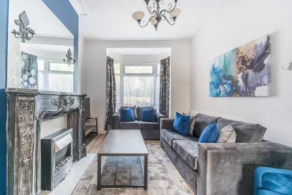 A living room with a fireplace, a sofa set, a coffee table, and a large abstract painting on the wall.