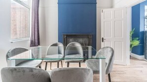 A dining area with a glass table and grey upholstered chairs, a blue accent wall, and a fireplace. - Near Hull Port House w/ Free Parking & Garden (Kingston upon Hull)