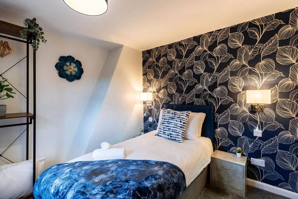 A bedroom with a bed, bedside tables, a wall-mounted lamp, and a decorative wall piece.