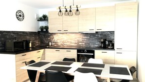 A modern kitchen with a dining area, featuring a stone backsplash, wooden cabinets, and a black countertop. - Logement Cosy Avec Parking (Aix-en-Provence)