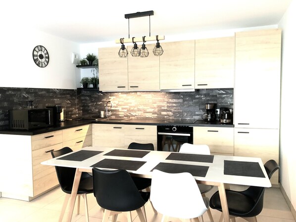 A modern kitchen with a dining area, featuring a stone backsplash, wooden cabinets, and a black countertop. - Logement Cosy Avec Parking (Aix-en-Provence)