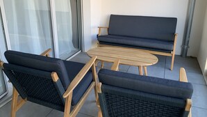 A balcony with a sofa and two chairs, a small round table, and a glass door with a sheer curtain. - Logement Cosy Avec Parking (Aix-en-Provence)