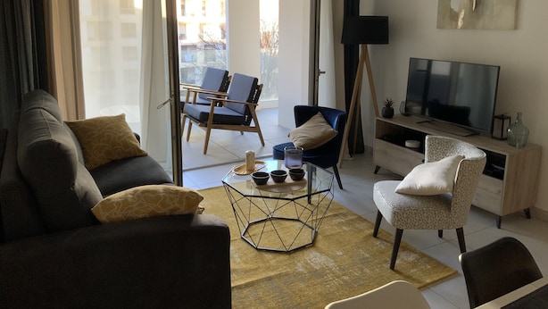 A modern living room with a sofa, armchairs, a coffee table, and a TV. - Logement Cosy Avec Parking (Aix-en-Provence)