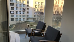 A balcony with two chairs and a small table, overlooking a residential area with modern buildings. - Logement Cosy Avec Parking (Aix-en-Provence)