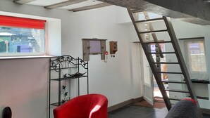 Una habitación con una silla roja, un sofá gris, una escalera y un ventanal con persiana roja.