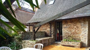 Un edificio de piedra con techo inclinado, un pequeño patio con mesa y sillas, y una ventana con vistas a los alrededores.