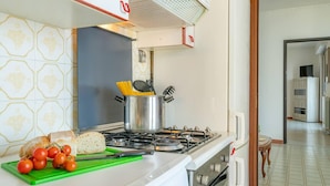 A kitchen with a gas stove, a pot with utensils, a loaf of bread, and tomatoes on a cutting board. - Charming 4-bed Apartment -lake Views & Balconies (Oliveto Lario)