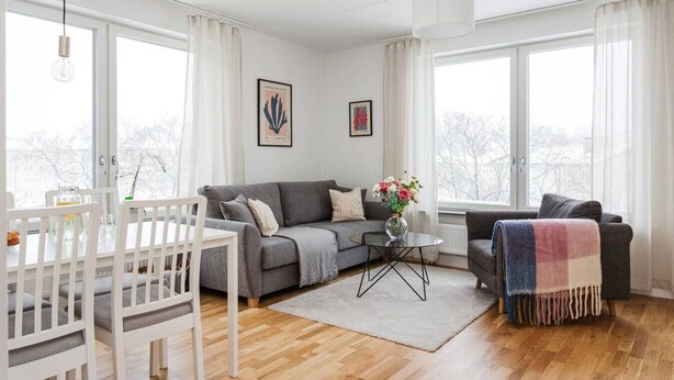 A modern living room with a grey sofa, white chairs, a coffee table, and a view through large windows. - Modern Scandinavian Home in Stockholm (Stockholms län)