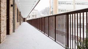 A covered corridor with brick walls, metal railings, and a snow-covered ground. - Modern Scandinavian Home in Stockholm (Stockholms län)