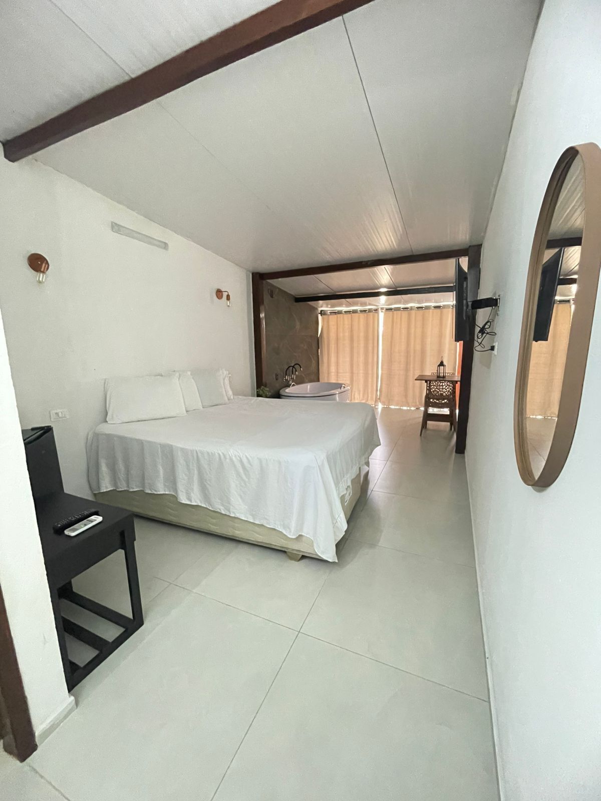 Una habitación de hotel con cama, escritorio, silla, televisor y ventana con cortinas.