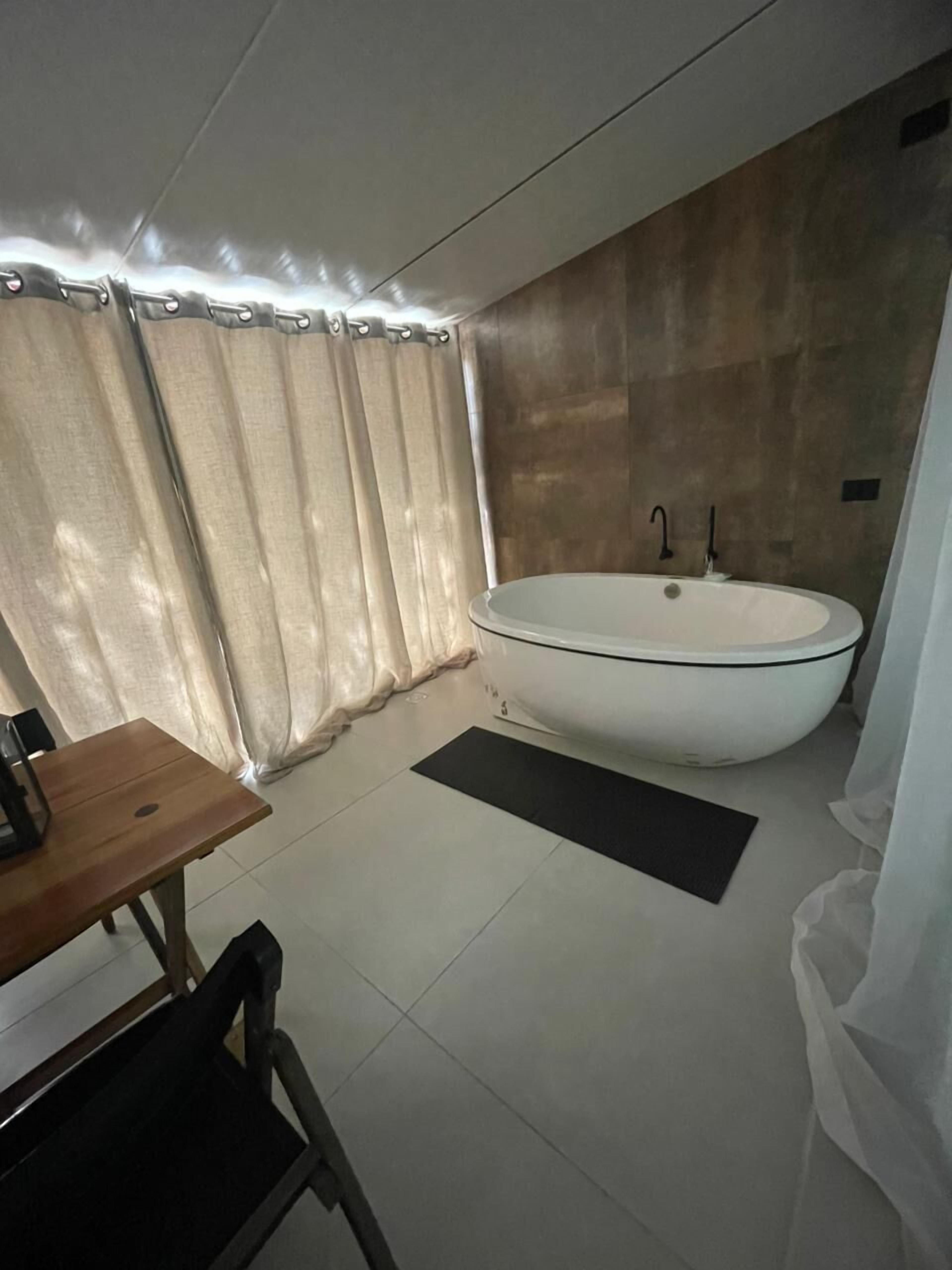 A modern bathroom with a freestanding bathtub, a wooden table, and a black mat on the floor.