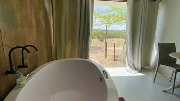 Un baño moderno con una bañera grande, una ducha y vistas a un paisaje árido por la ventana.