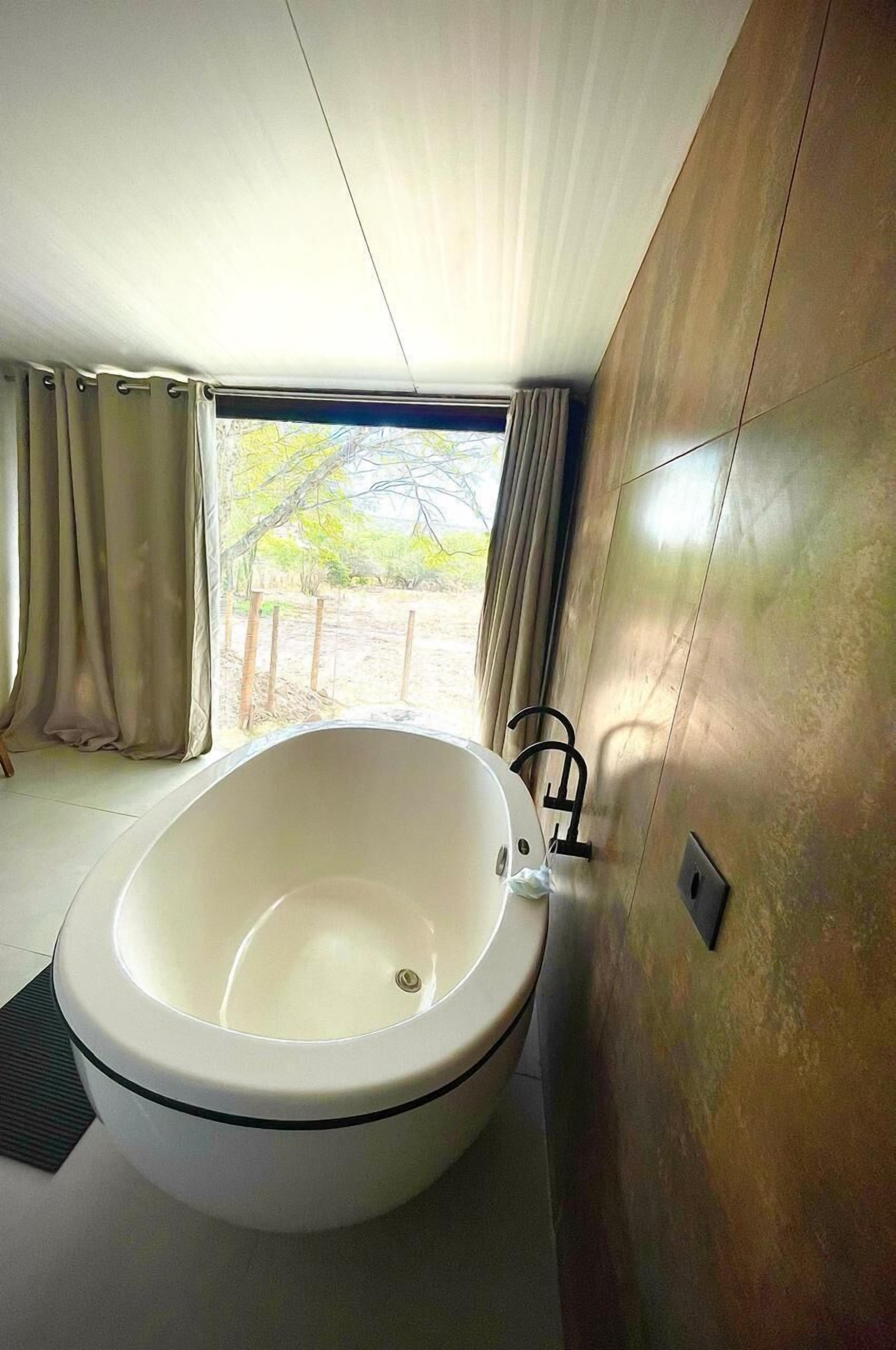 Un bagno moderno con una vasca da bagno indipendente, una finestra con tende e vista sull'esterno.
