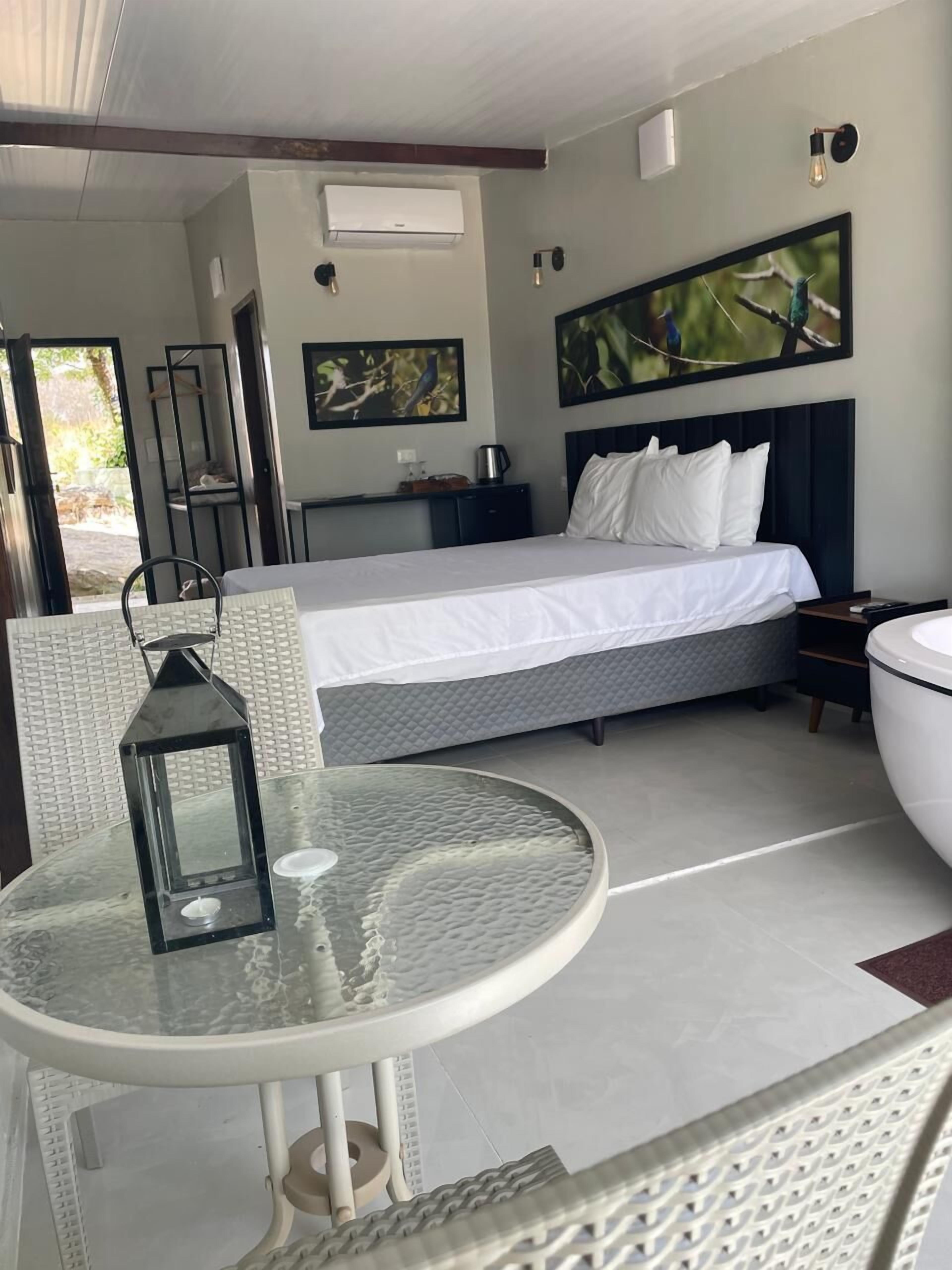 A hotel room with a bed, a small table with a lantern, a nightstand, and a painting on the wall.