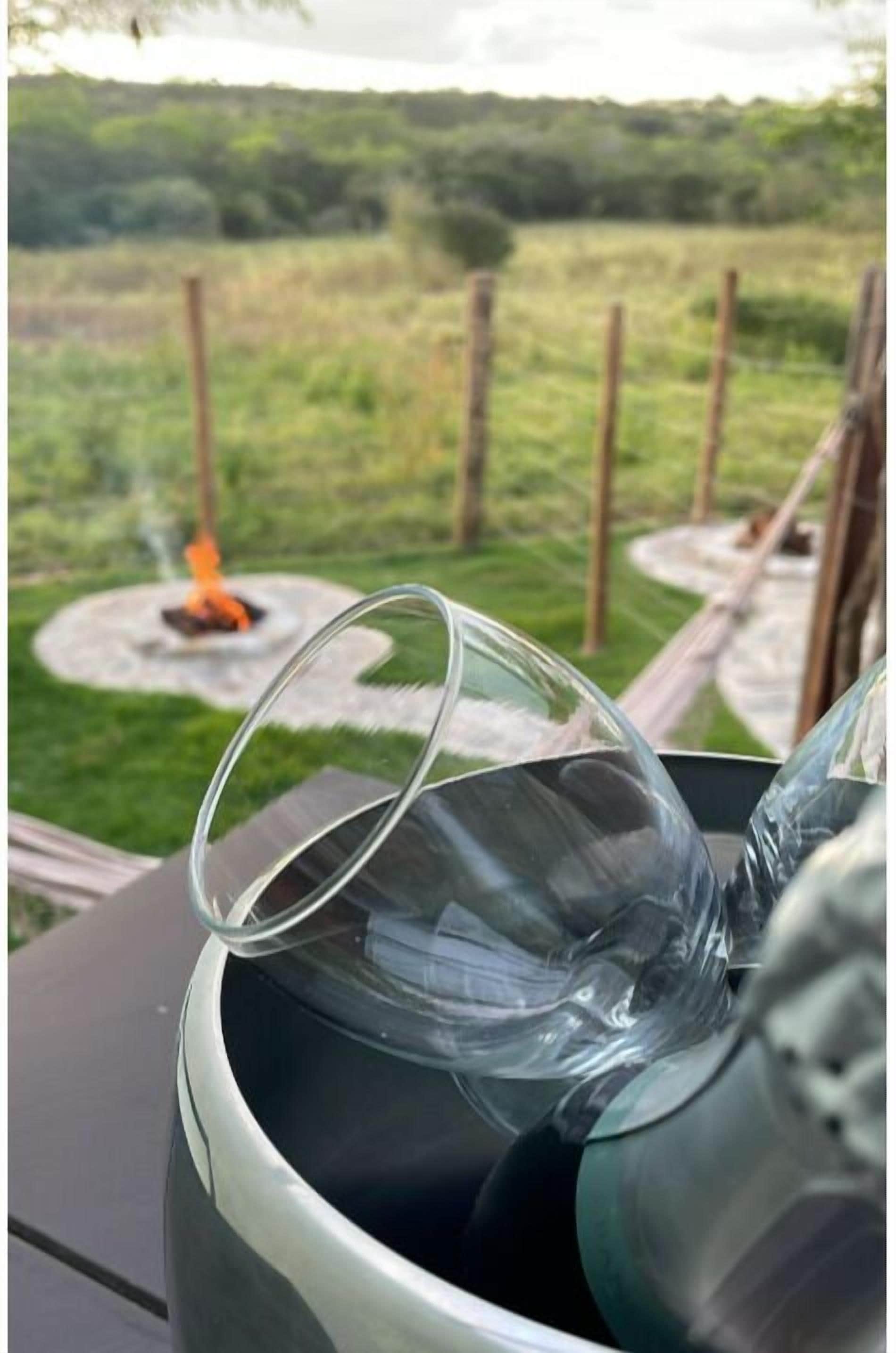 A glass object on a table with a view of a grassy field and a fire pit in the background.