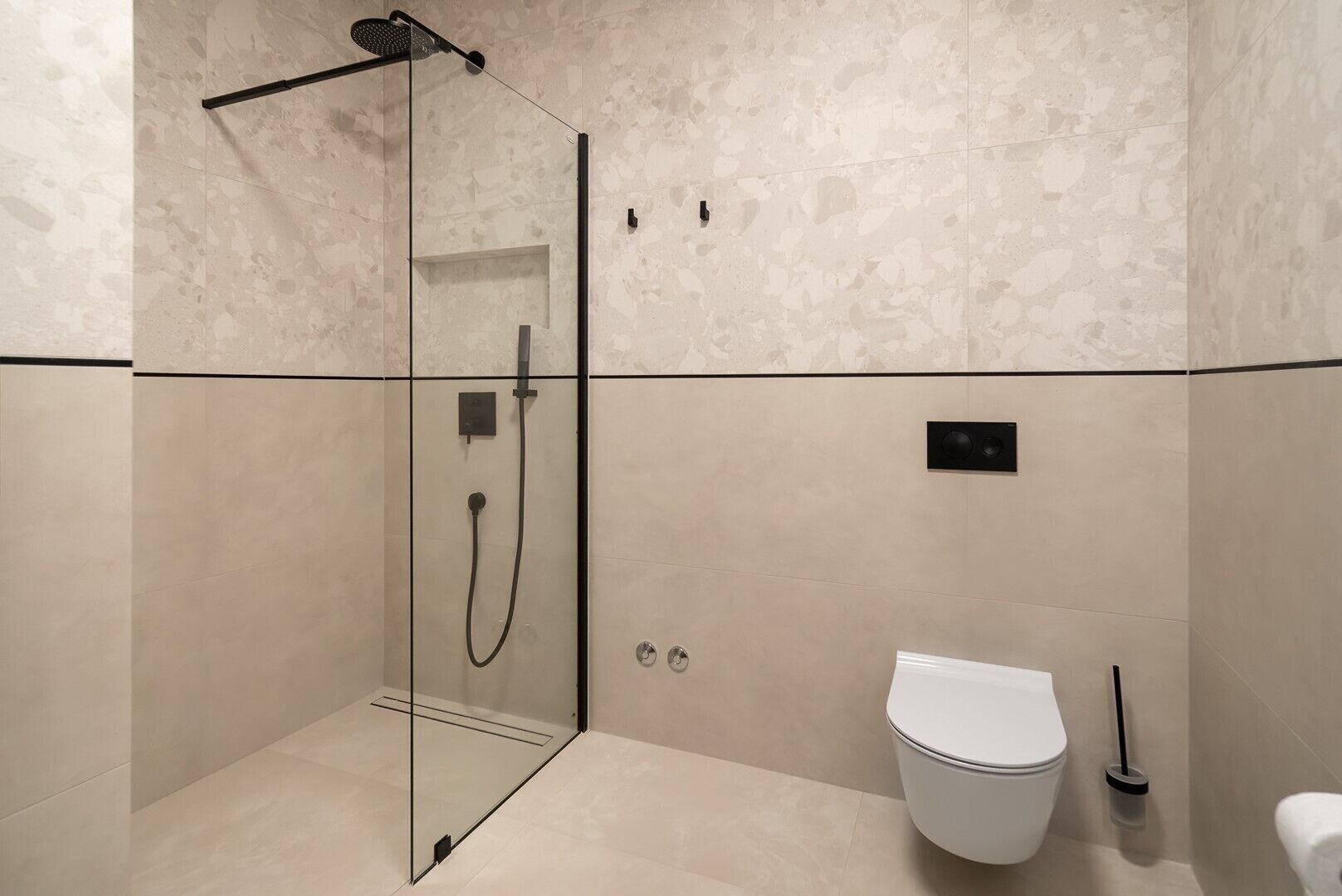 A modern bathroom with a glass-enclosed shower, a white toilet, and a black handheld showerhead.