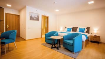 Une chambre à coucher avec un lit, deux fauteuils bleus, une petite table ronde, un plancher en bois et une table de chevet avec une lampe.