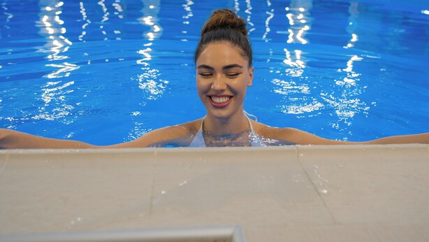 Una piscina interior con agua cristalina, rodeada de suelo de baldosas y techo de cristal.