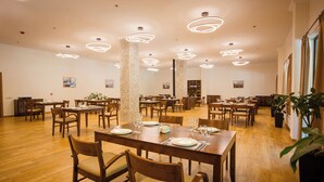 Un comedor amplio con varias mesas y sillas de madera, iluminación colgante moderna y plantas en macetas.