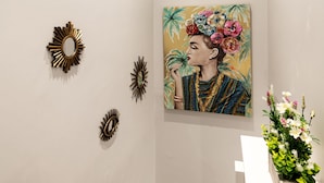 A room with a white wall, a painting of a woman with a floral headpiece, and decorative wall mirrors.