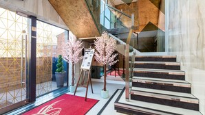 A modern hotel lobby with a glass staircase, a red carpet, and decorative cherry blossom trees. - Apartment 1 of Address Apartments (Gillingham)