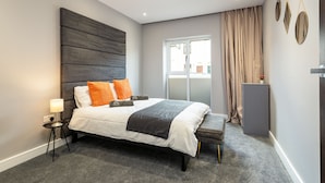 A modern bedroom with a large bed, bedside tables, a bench, a nightstand, and a window with curtains.