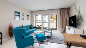 A modern living room with a teal sofa, a coffee table, and a TV on a stand.
