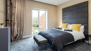 A modern bedroom with a large bed, a bench, a dresser, and a window with curtains. - Apartment 4 of Address Apartments (Gillingham)
