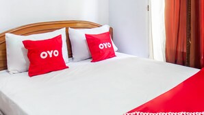 A bed with white bedding and two red pillows with "OYO" text, a wooden headboard, and a white wall with a light switch. - OYO Life 93409 Anugrah House (Mataram)
