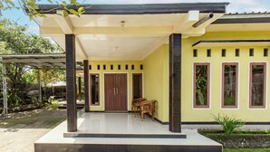 A yellow building with a covered porch, wooden doors, and a small table. - OYO Life 93409 Anugrah House (Mataram)