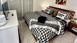 Une chambre à coucher bien rangée, avec une couvre-lit à carreaux, une table de chevet dotée d’une lampe et une œuvre d’art accrochée au mur.
