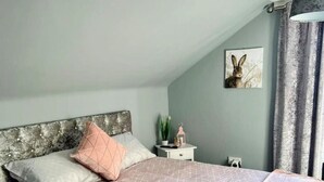A bedroom with a bed, pillows, a bedside table, a wall-mounted picture, and a window with curtains.