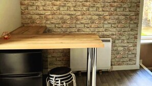 A room with a brick wall, a wooden table, a black chair, and a white radiator.