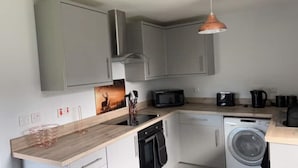 A compact kitchen with grey cabinets, a wooden countertop, a microwave, a coffee maker, and a washing machine.