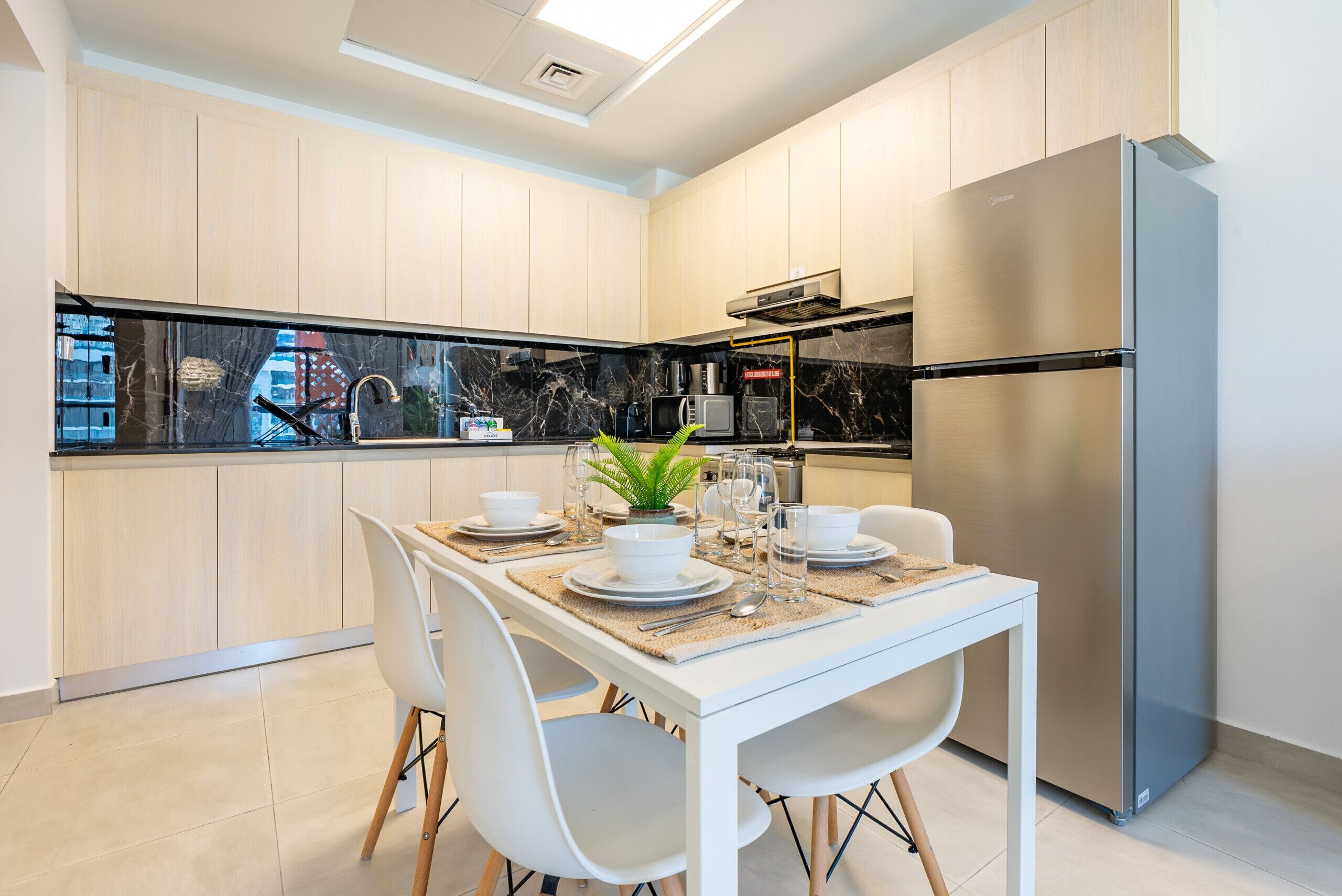 Een moderne keuken met een eethoek, met een roestvrijstalen koelkast, een zwart-wit marmeren spatwand en een eettafel met witte stoelen.