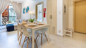 A modern dining area with a table set for four, a sofa, and a view of the city. - Community View 1BR, Just Next to the Park and a Short Walk to the Bus Stop (Dubai)