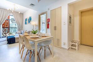 A modern dining area with a table set for four, a sofa, and a view of the city. - Community View 1BR, Just Next to the Park and a Short Walk to the Bus Stop (Dubai)