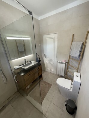 Een moderne badkamer met een douchecabine van glas, een wastafel met spiegel, een toilet en een handdoekrek.