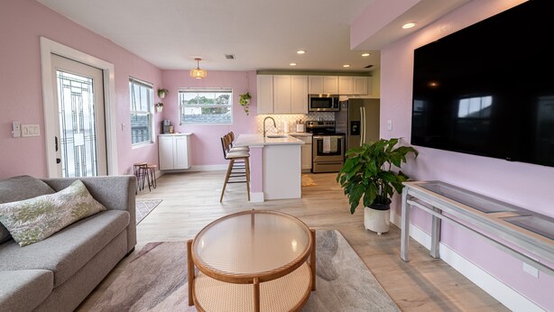 A modern living room with a sofa, a round table, and a TV. There is a kitchen in the background with a microwave, oven, and sink. - Tropical Treetop Hideaway Just a Short Walk to Beach (Lake Worth Beach)