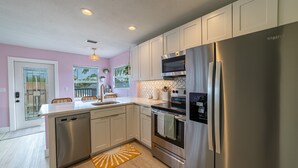 A modern kitchen with stainless steel appliances, white cabinetry, and a wooden floor. - Tropical Treetop Hideaway Just a Short Walk to Beach (Lake Worth Beach)