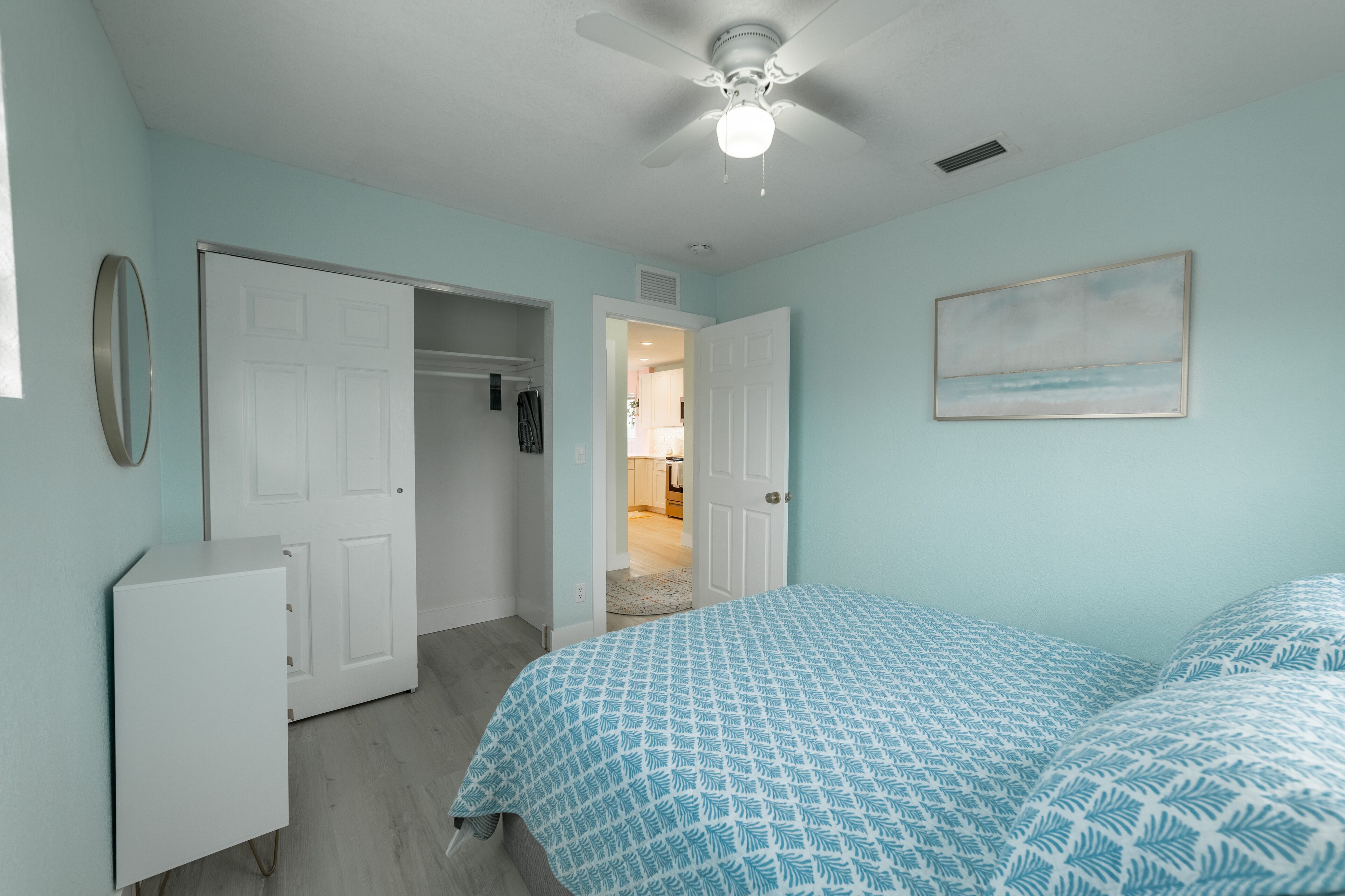 Quarto com cama, guarda-roupa, ventilador de teto e um quadro na parede.