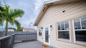 A wooden deck with a palm tree, a door with a glass panel, and a window with a view of the sky. - Tropical Treetop Hideaway Just a Short Walk to Beach (Lake Worth Beach)