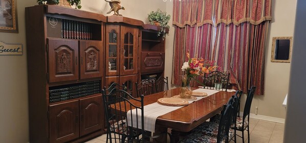 A dining room with a wooden table set for four, surrounded by chairs. A large wooden cabinet with glass doors is to the left, and a vase with flowers is on the table. - Gorgeous 5 bedroom home w/ pool. Close to Destin Beaches. No cleaning fee! (Niceville)