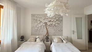 A bedroom with two beds, a wall-mounted artwork, and a door leading to another room. - Spacious 95 sqm newly renovated vacation home with breathtaking views (Menaggio)