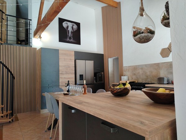 A modern kitchen with a wooden island, a hanging light fixture, and a framed elephant picture on the wall.