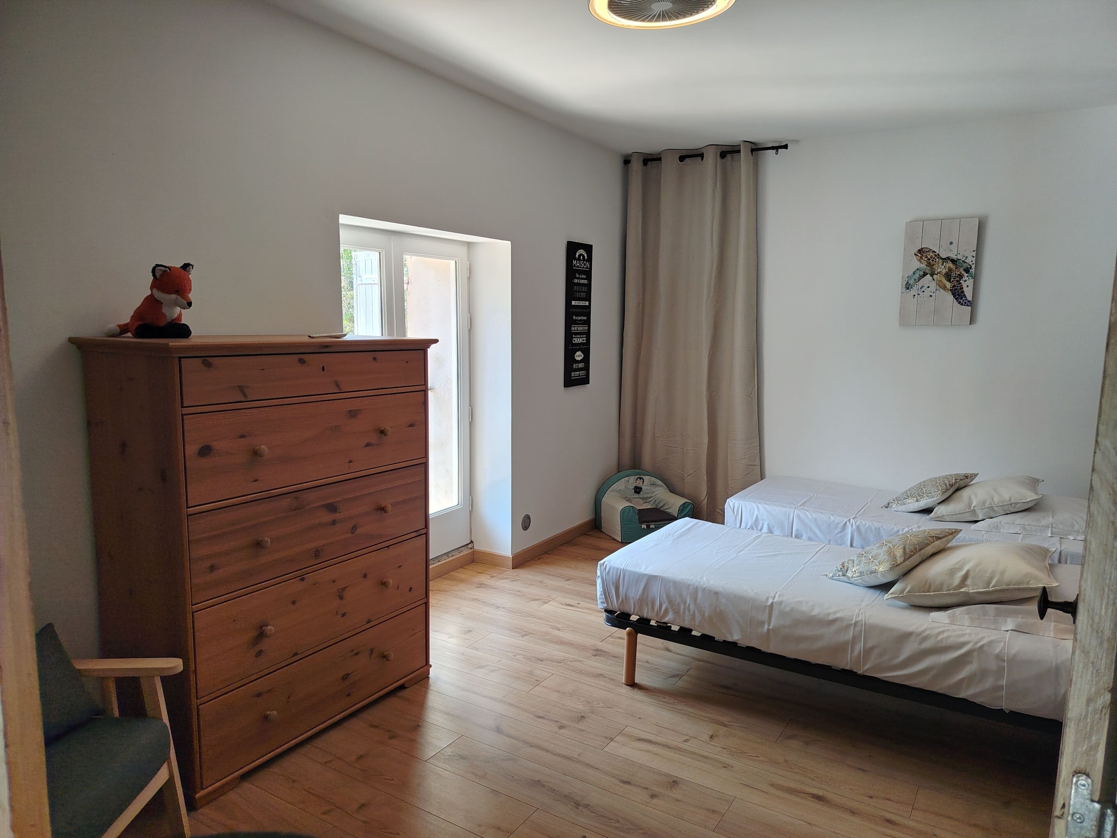 Una camera da letto con un comò in legno, un letto con biancheria bianca, una finestra con tende e un'opera d'arte appesa al muro.